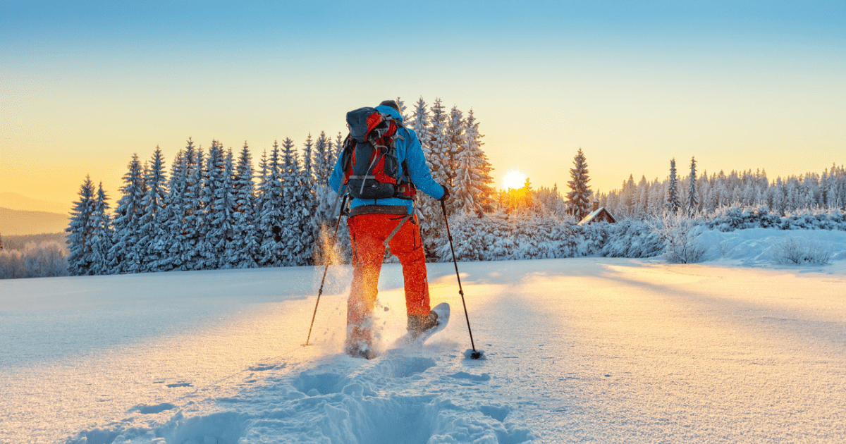 A person walking in the snow in snow gear with skis and a bug out bag.