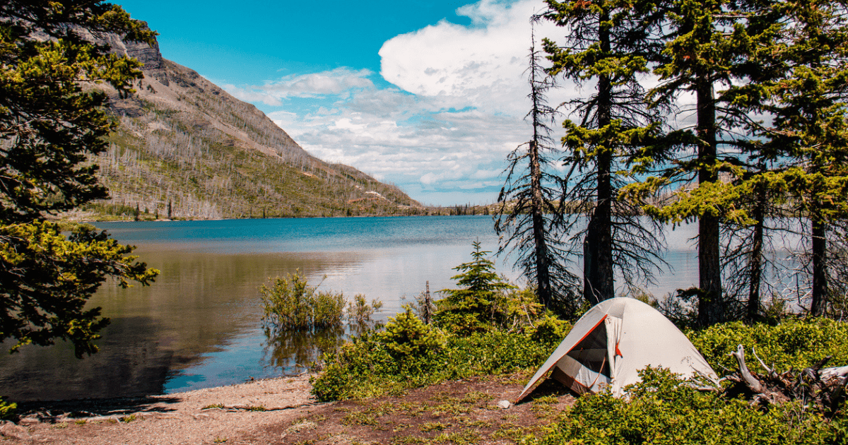 A tent by a blue lake in the forest.