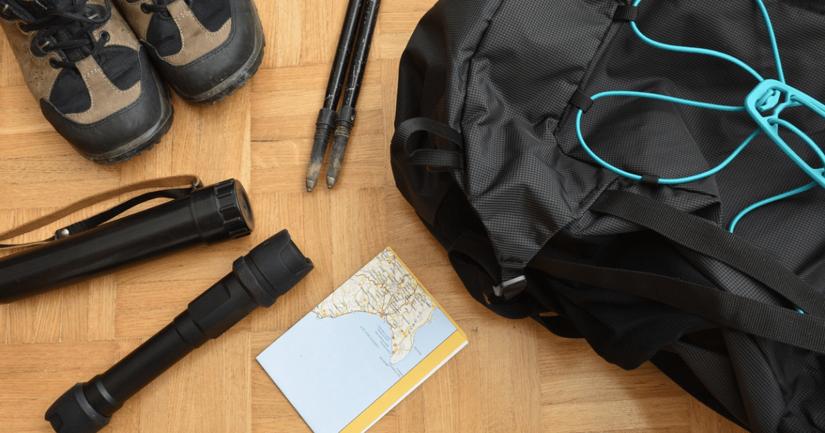 A backpack, flashlight, shoes, and other items laying on floor to be packed into bug out bag.