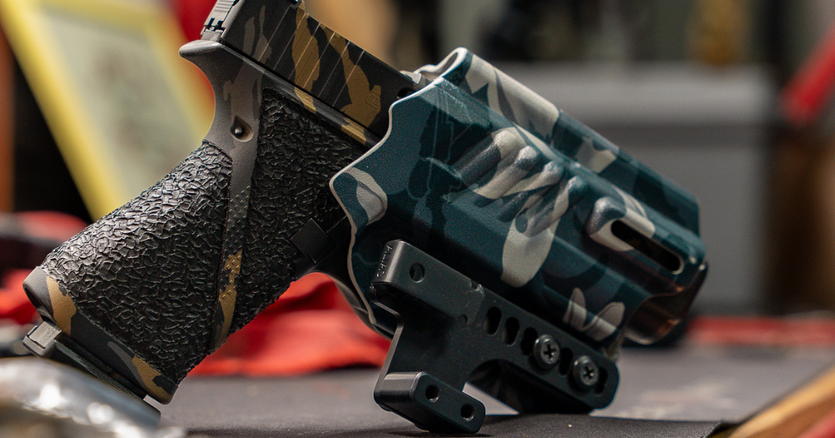 A green holster with an Alias Holster Clip attached resting on a table.